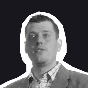 A grayscale portrait of a man in a checkered shirt and jacket, looking forward against a dark background, embodying.
