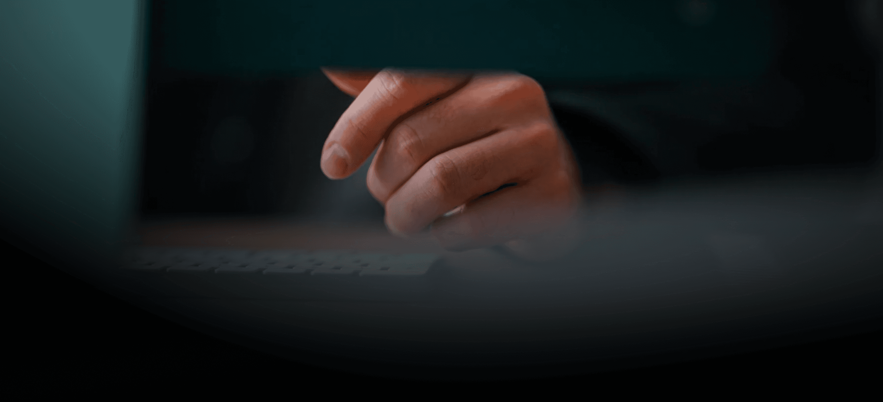 A person's hand with warm, natural skin tones hovers above a dark keyboard, illuminated by a soft cool blue light from a.