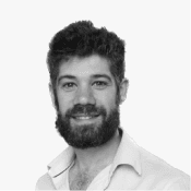 A black and white headshot of a smiling man with a neatly trimmed beard and curly hair, exuding a professional and.