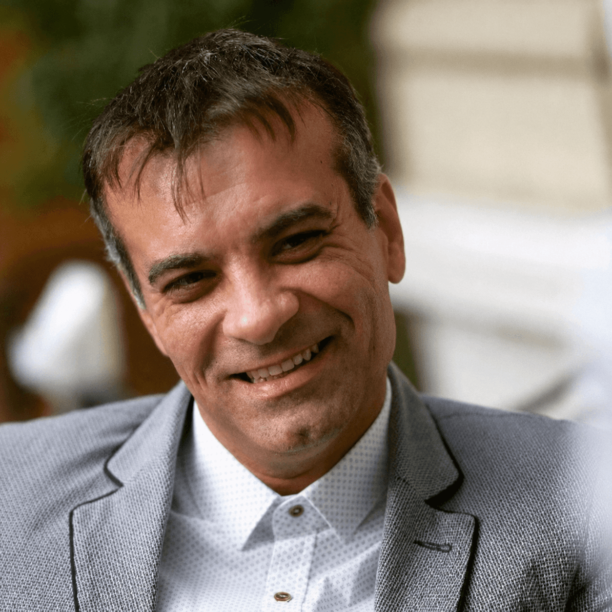 Smiling man in a light grey blazer and patterned shirt