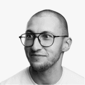 A smiling man with a shaved head and stylish round glasses looks upward, embodying the innovative spirit of Birdie.
